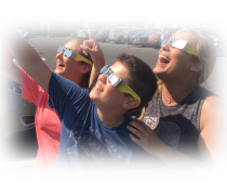 Three people wearing solar eclipse viewing glasses look up towards the sun.