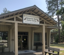 Image of front of building with double glass doors and sign above doors that says "Richard S Bolt Visitor Center" with a bench and sidewalk in foreground