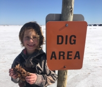 a young child holds a large crystal cluster standing next to a sign reading Dig Area