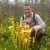 Man in a forest crouched over and smiles, next to bright-yellow pitcher plants.