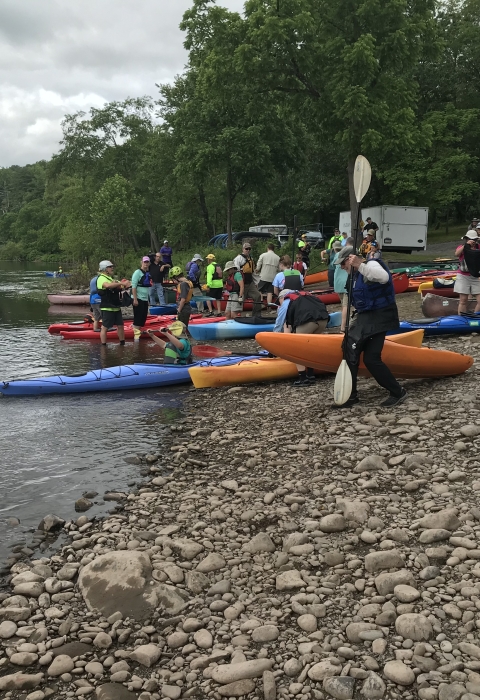 A group of people prepare to launch kayaks on a cobble river beach