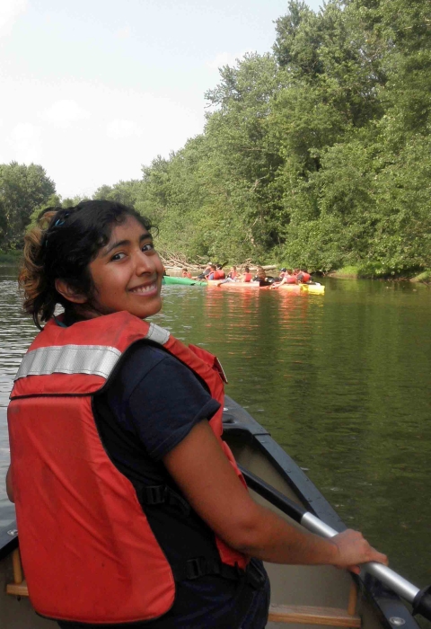 A latina woman wearing an orange personal flotation device canoeing on a river