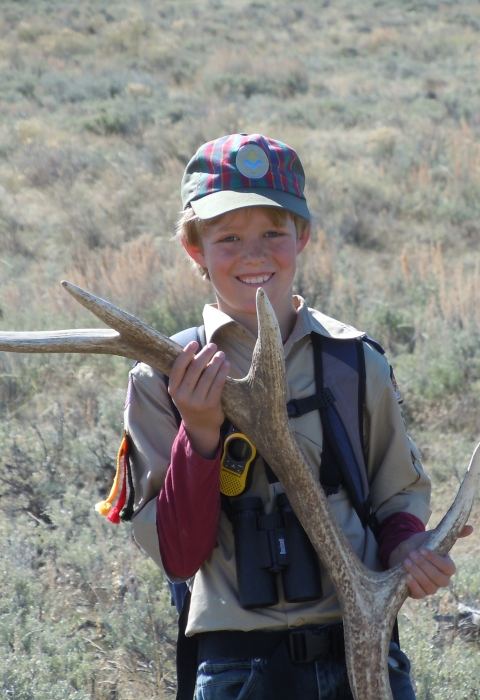 A young boy holing a huge antler shed that's about the same size as he is