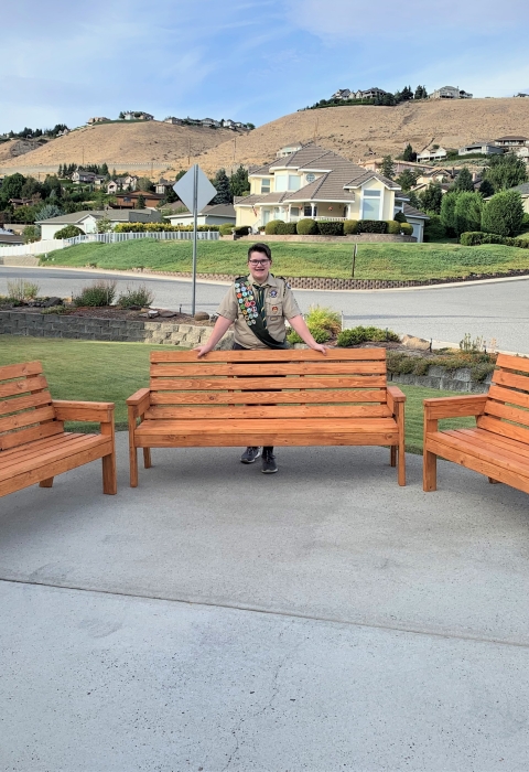 A youth volunteer in his boy scout uniform poses behind the wooden benches he made for Leavenworth NFH