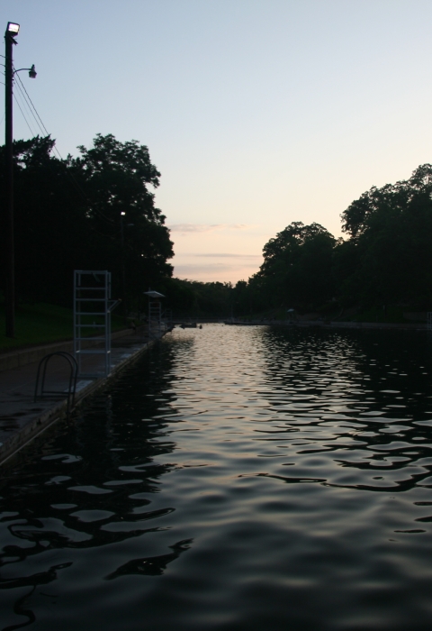 Barton Springs pool is shown against a background of a sunset.