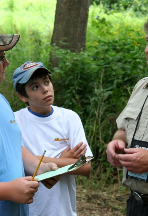 A man in a US Fish & Wildlife Service uniform talking to children in a forest