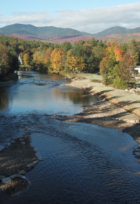 An aerial view of a river surrounded by trees with fall foliage