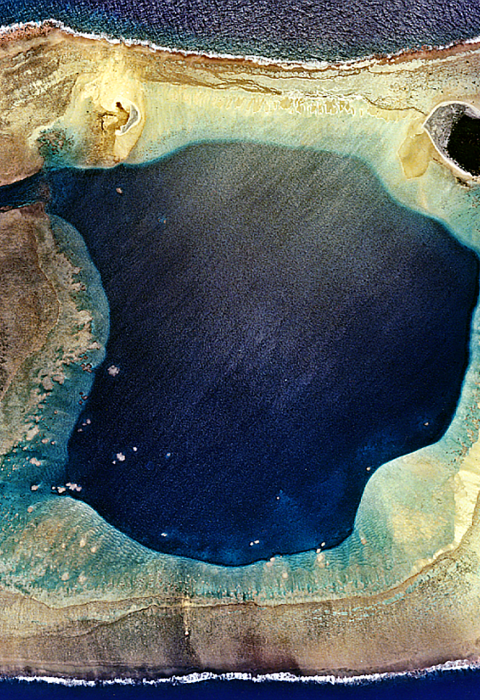 A satellite view of Wake Atoll. It is shaped like a square with an entrance to the sea to the left that opens up to a large bay. 