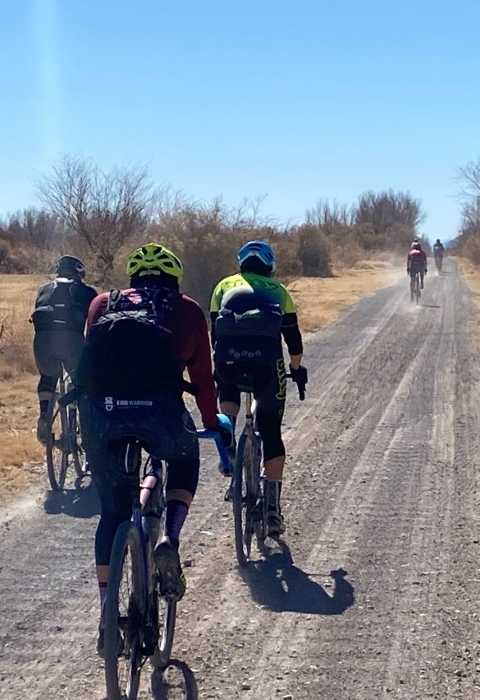 cyclists ride along a dirt road in the desert