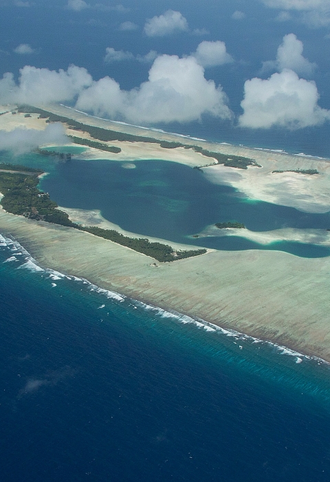 Aerial view of an island atoll surrounded by sandy reef in the deep blue ocean