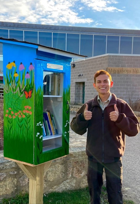 Ranger Logan Sauer stands next to the new tiny library outside the visitor center. The library is painted with native flowers.