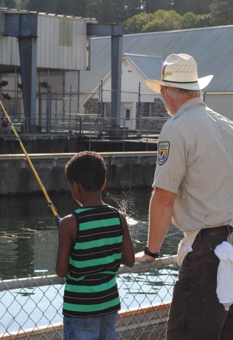 An adult showing a young person to fish over a railing at a fish hatchery.
