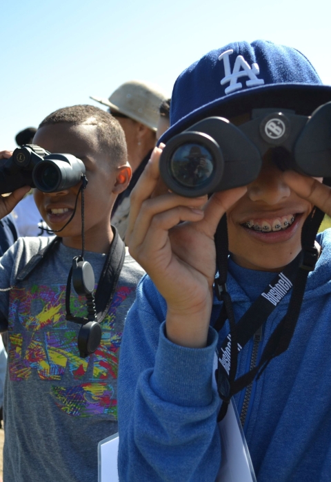Smiling children look through binoculars on a sunny day.
