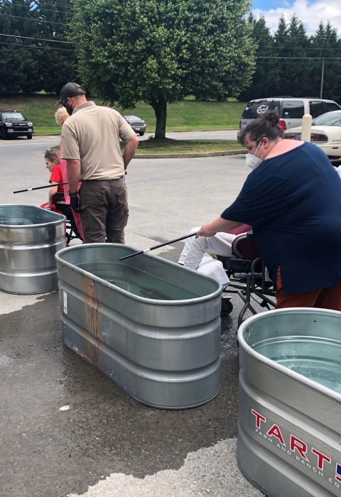 People fishing out of small, galvanized stock tanks in a parking lot