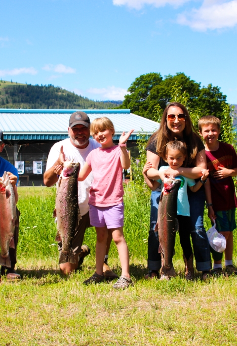 A group of adults with children show off the large trout they have just caught on a sunny June day.