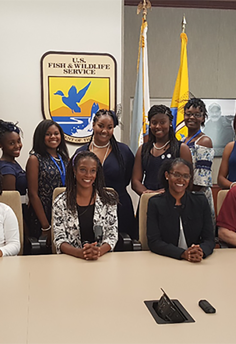 FWS employees and Zeta Phi Beta Sorority sitting and stand with official Service logo and flags in the background. 