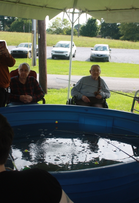 Elderly people sitting around a holding tank with fishing poles