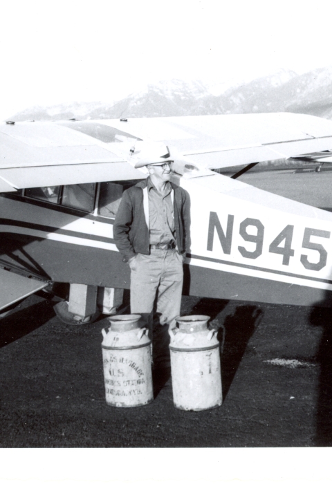 A man stands next to a small aircraft with milk cans of fish to release