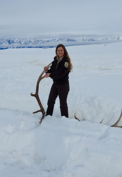 A woman stands in snow holding the end of an antler
