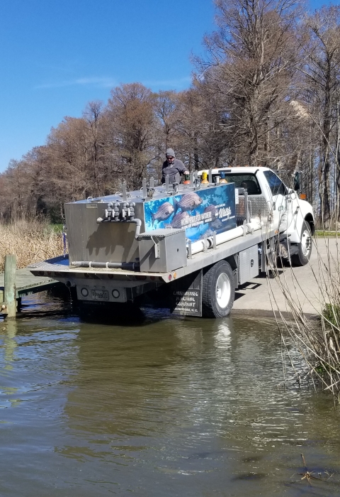 A truck with a large metal tank banks into a boat launch.