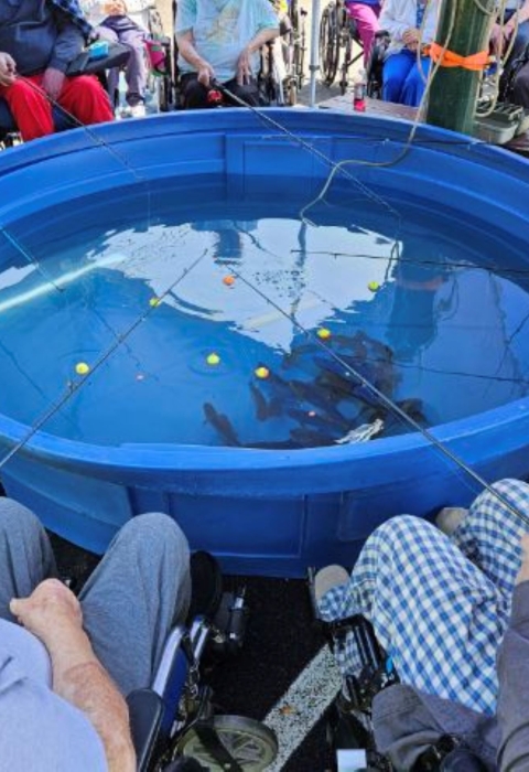 Elderly people gathered around a blue tub with fishing poles