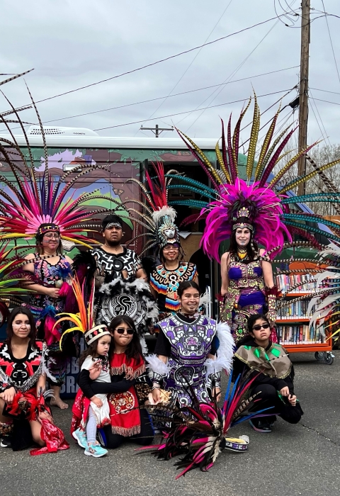 People in tradition dress are posed for a picture in a group. The outfits are very colorful and they are wearing feathered head-dresses. 