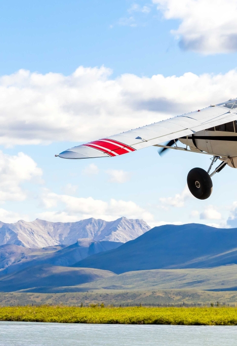 bush plane in the air over river and mountains