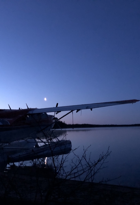 Airplane sitting on water at night with the moon in the background