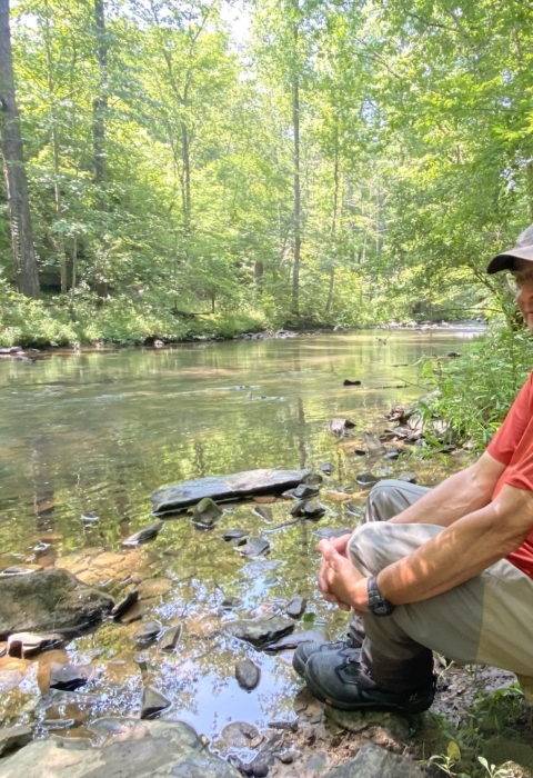 A man sitting alongside a creek.