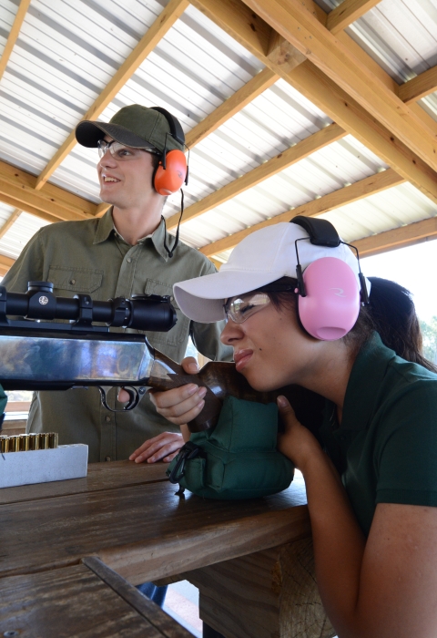 Target shooter aims rifle at targets at firearm range. 