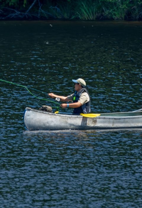 Two fly fishing academy campers fishing from a canoe on a lake. 