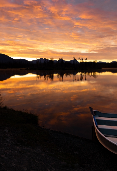 A sunset on a lake with a rowboat on shore