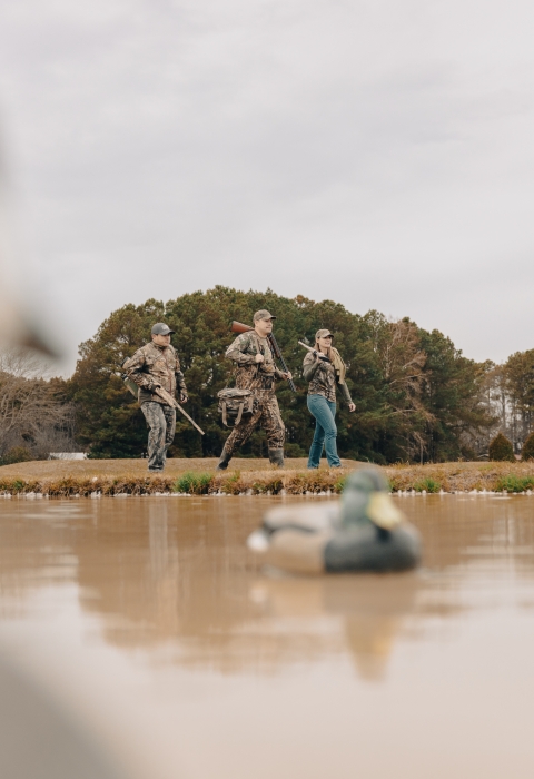 Three hunters dressed in camouflage walking past duck decoys. 