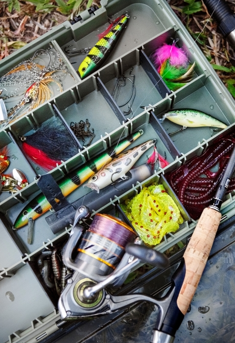 An open tackle box full of colorful fishing lures, hooks, and a fishing rod. 