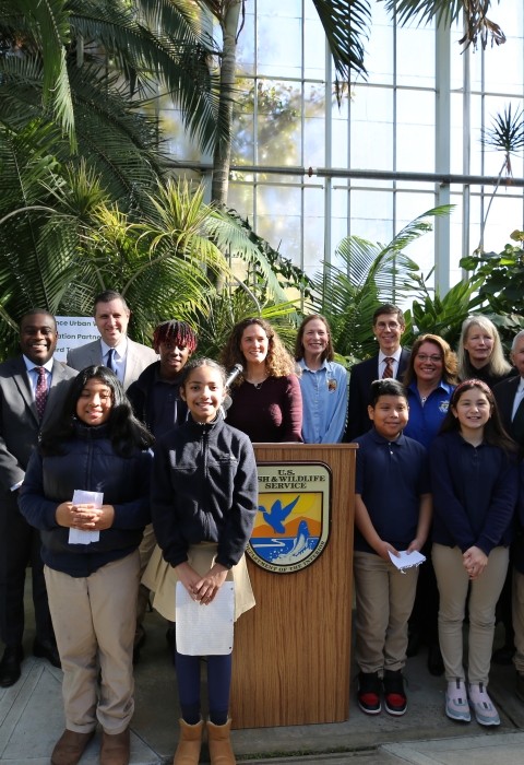 Group photo of adults and youth smiling. A U.S. Fish and Wildlife Service logo can be seen on a podium in the center of the photo