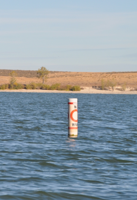 A line of separated buoys out on a lake with text that reads “No Wake” and an open orange circle in between.