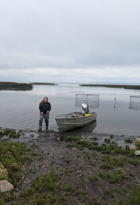 person stands on a lake shoreline with wire traps in the background