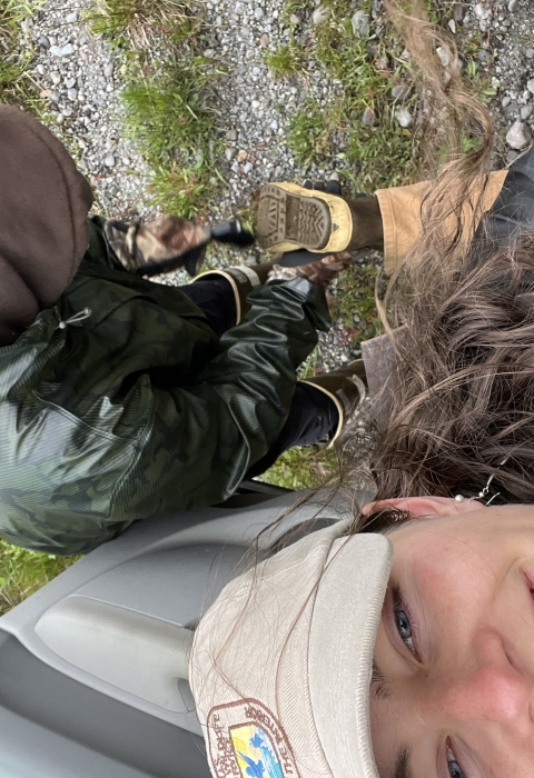 Biologist smiling while lifting a boot up to have friend clean dirt out of tread. 