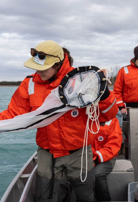 Biologists on a boat wearing float coats. One is holding a plankton tow net on the side to sample for invasive mussels.