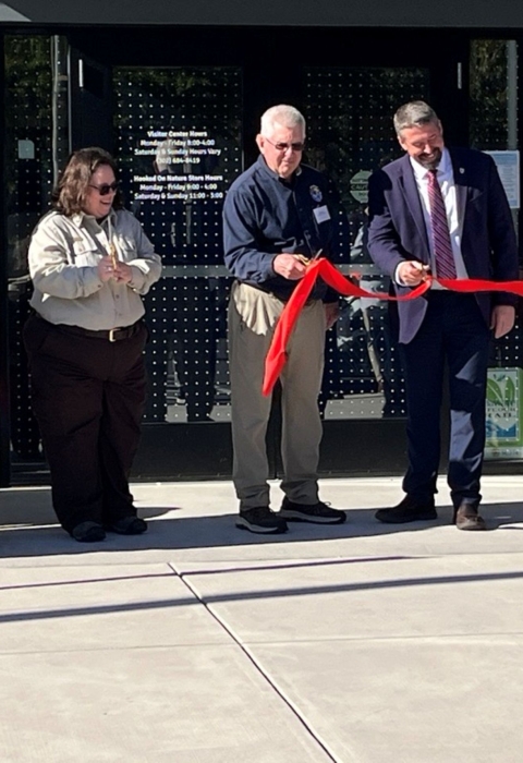 Men and women hold scissors to cut a large red ribbon.