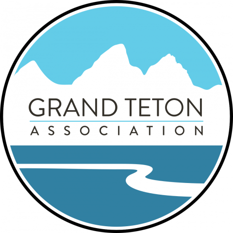 Black outlined circle with blue mountain depicted inside with text that reads "Grand Teton Association"