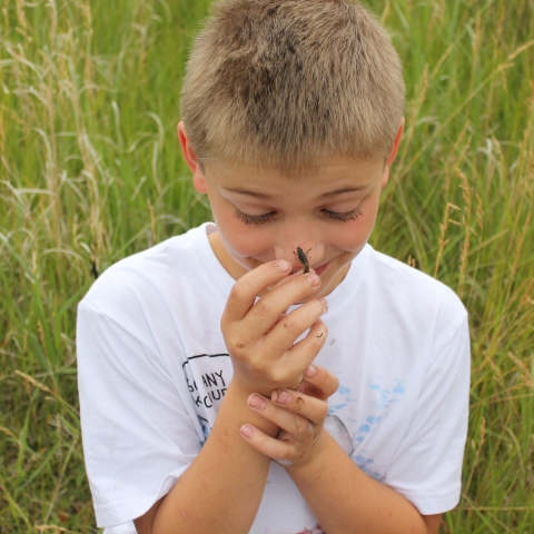 A smiling boy lets a crayfish crawl on his nose