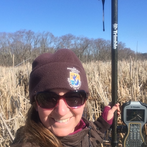 Wildlife Biologist Stephanie Koch standing in a wetland with a scientific device