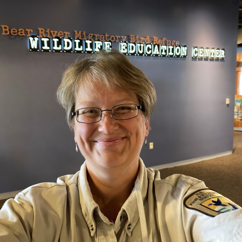 Woman in uniform in front of a sign that reads Bear River Migratory Bird Refuge Wildlife Education Center