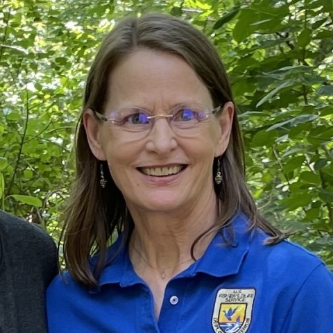 a smiling woman with blond hair and blue eyes wearing a blue polo shirt with the Fish and Wildlife Service logo