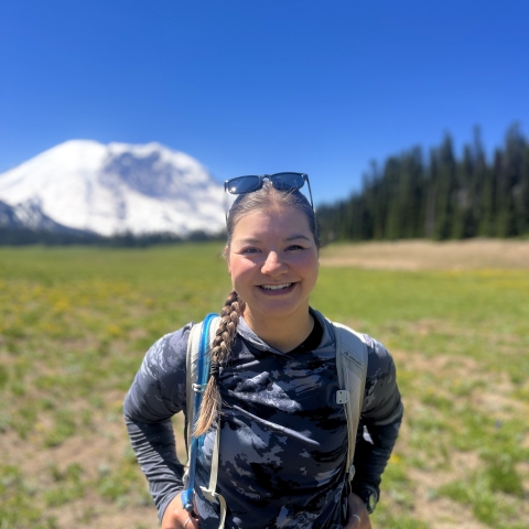 Hannah Ferwerda standing in a field with Mount Rainier in the background with trees and blue sky.