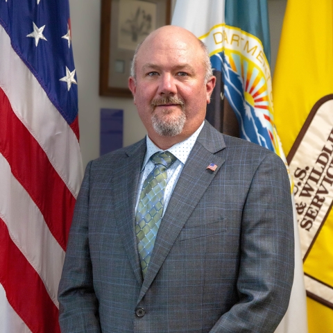 man in suit in front of US, FWS flags