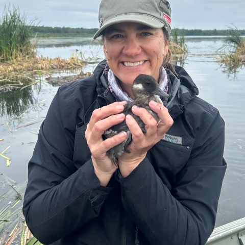 A woman wearing a green ball cap holds a duck.