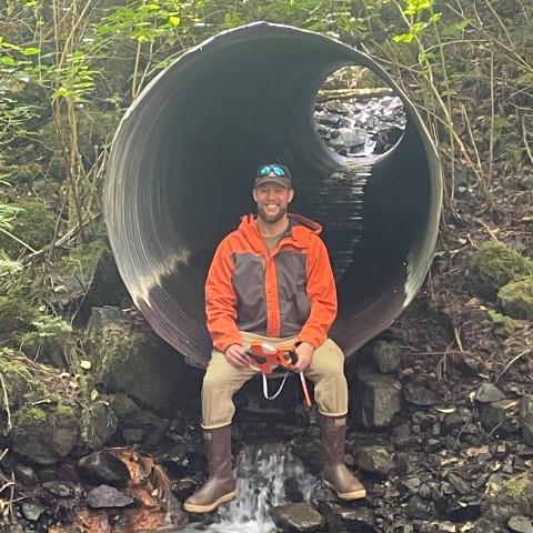 Andy Stevens sitting at the end of a culvert with water running through it. 