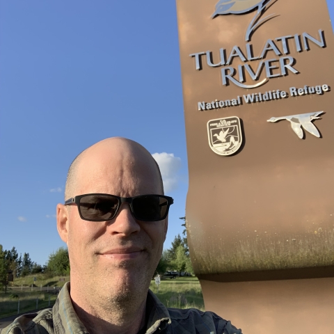 a man standing outside in front of a sign for Tualatin River National Wildlife Refuge
